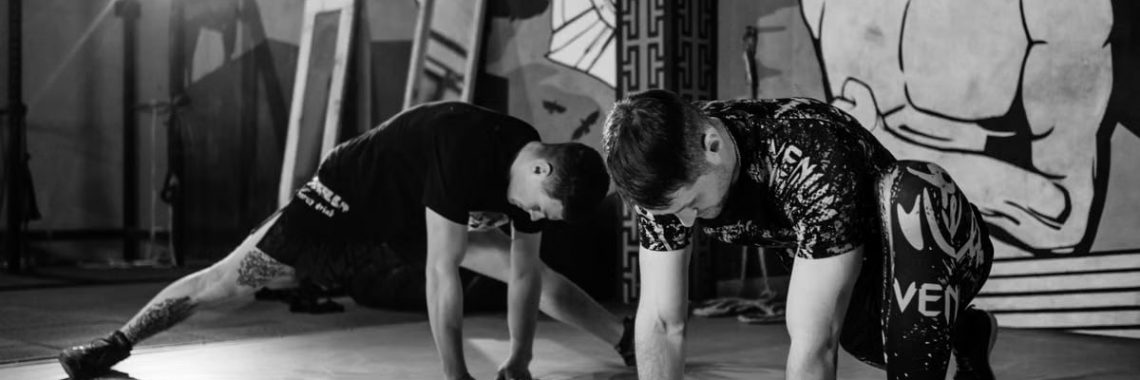 Two men stretching inside a gym, preparing for MMA training in a grayscale setting.