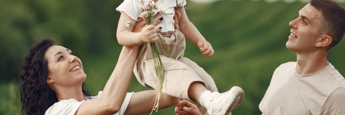 Happy family enjoying playful outdoor moment, lifting child in summer day.